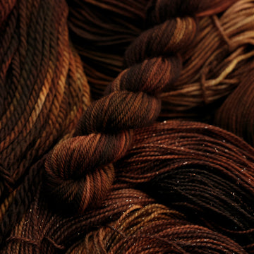 A dark brown colored DK mini yarn that has some lighter tones of brown and different shades. There are unwound versions of this skein in different weights underneath this skein.