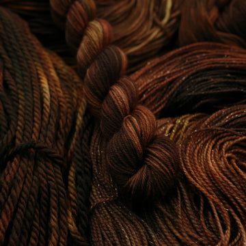 A dark brown colored Fingering mini yarn that has some lighter tones of brown and different shades. There are unwound versions of this skein in different weights underneath this skein.