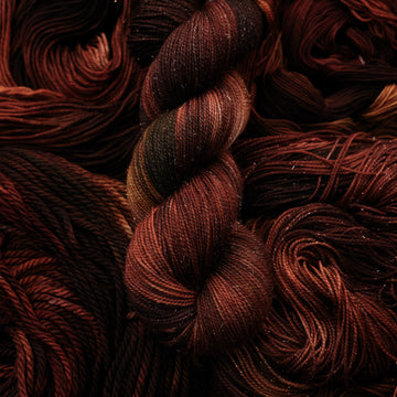 A dark brown colored Sparkle yarn that has some lighter tones of brown and different shades. There are unwound versions of this skein in different weights underneath this skein.