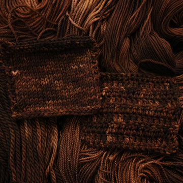 A dark brown colored Crochet and Knit swatches that have some lighter tones of brown and different shades. There are unwound versions of this skein in different weights underneath this skein.
