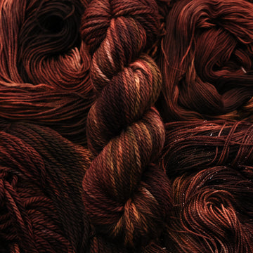 A dark brown colored Bulk yarn that has some lighter tones of brown and different shades. There are unwound versions of this skein in different weights underneath this skein.
