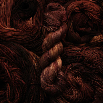 A dark brown colored Silk yarn that has some lighter tones of brown and different shades. There are unwound versions of this skein in different weights underneath this skein.