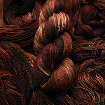 A dark brown colored Worsted yarn that has some lighter tones of brown and different shades. There are unwound versions of this skein in different weights underneath this skein.