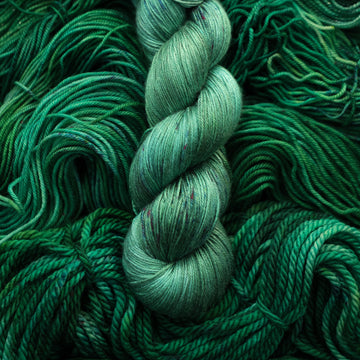 An emerald green colored Silk yarn that is on top of the same colored unwound yarn in different weights.