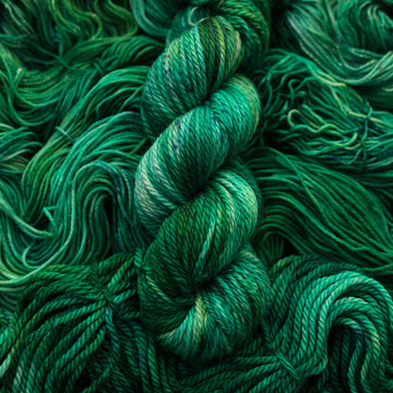 An emerald green colored Bulky yarn that is on top of the same colored unwound yarn in different weights.