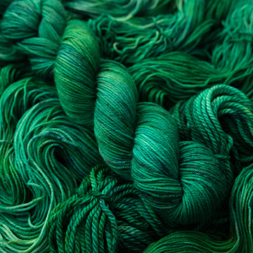 An emerald green colored DK yarn that is on top of the same colored unwound yarn in different weights.