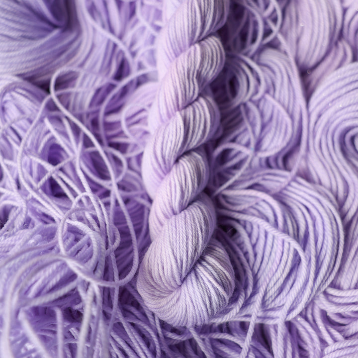 Fingering mini yarn colored a light violet color on top of unwound skeins of this same color way.