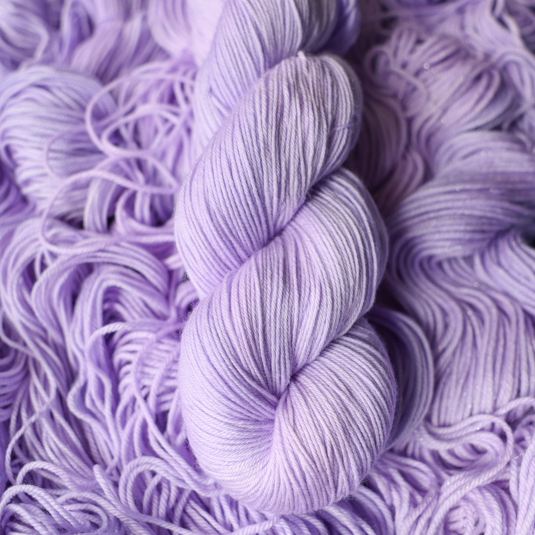 Fingering yarn colored a light violet color on top of unwound skeins of this same color way.