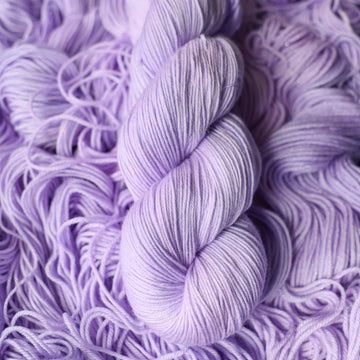 Fingering yarn colored a light violet color on top of unwound skeins of this same color way.