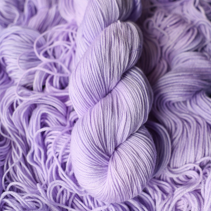Fingering yarn colored a light violet color on top of unwound skeins of this same color way.