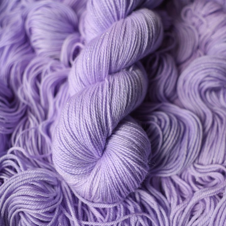 Sparkle fingering yarn colored a light violet color on top of unwound skeins of this same color way.
