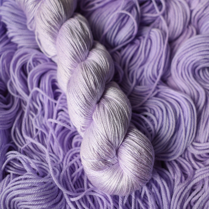 Silk yarn colored a light violet color on top of unwound skeins of this same color way.