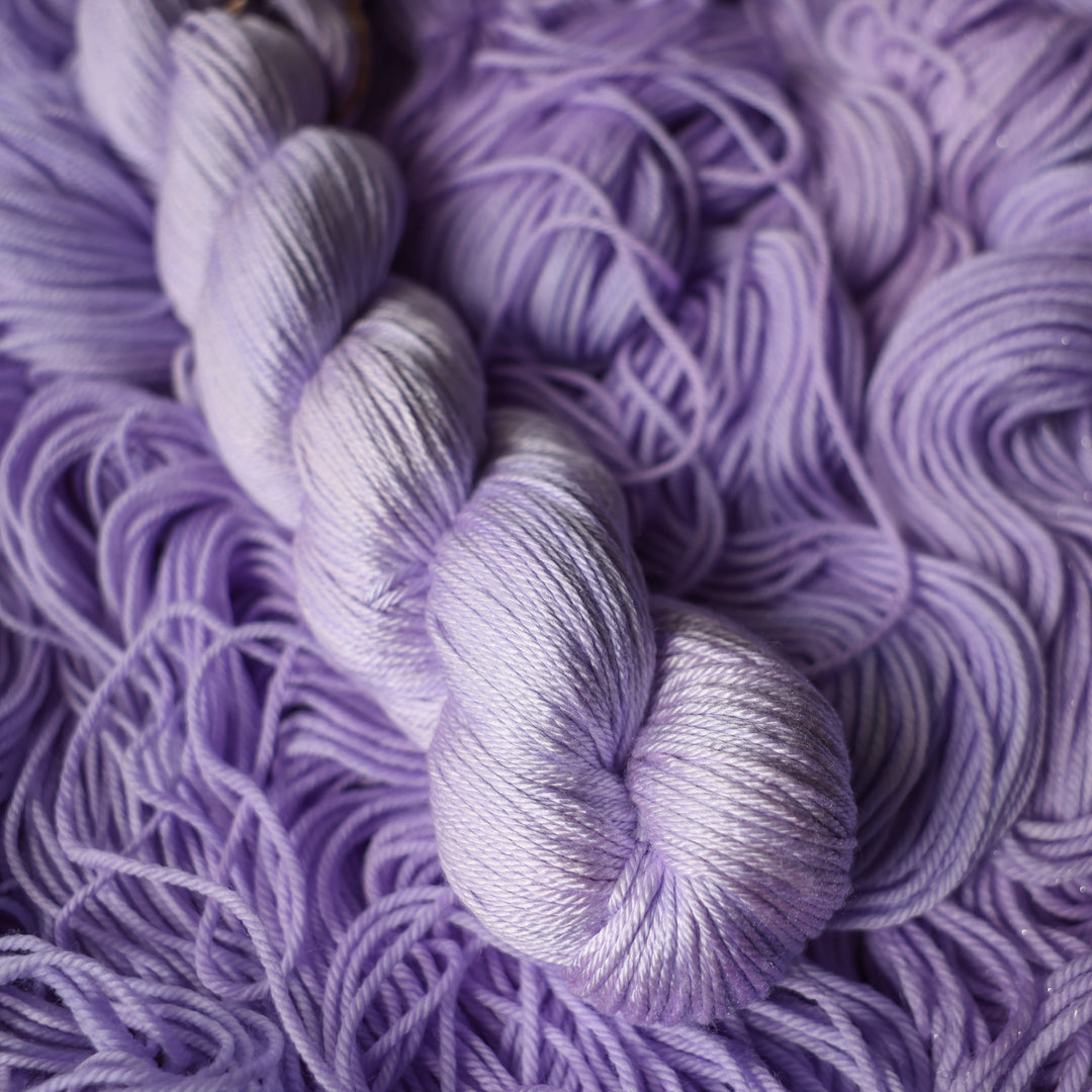 Silk DK yarn colored a light violet color on top of unwound skeins of this same color way.