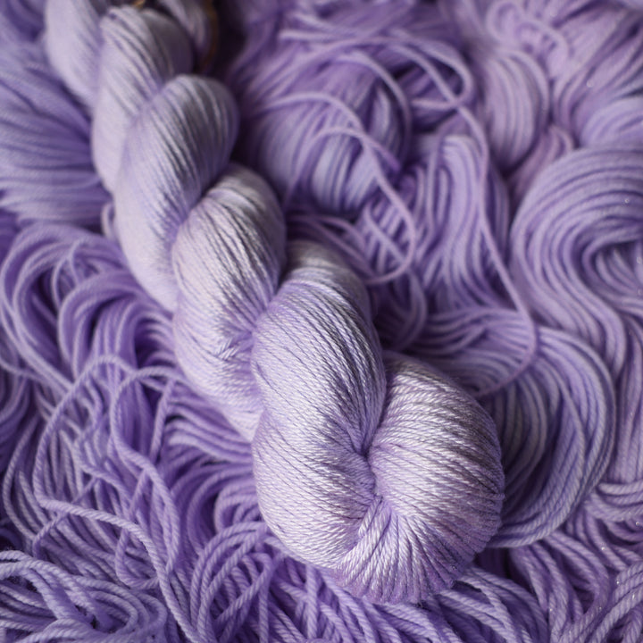 Silk DK yarn colored a light violet color on top of unwound skeins of this same color way.