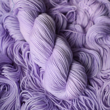 Sport yarn colored a light violet color on top of unwound skeins of this same color way.