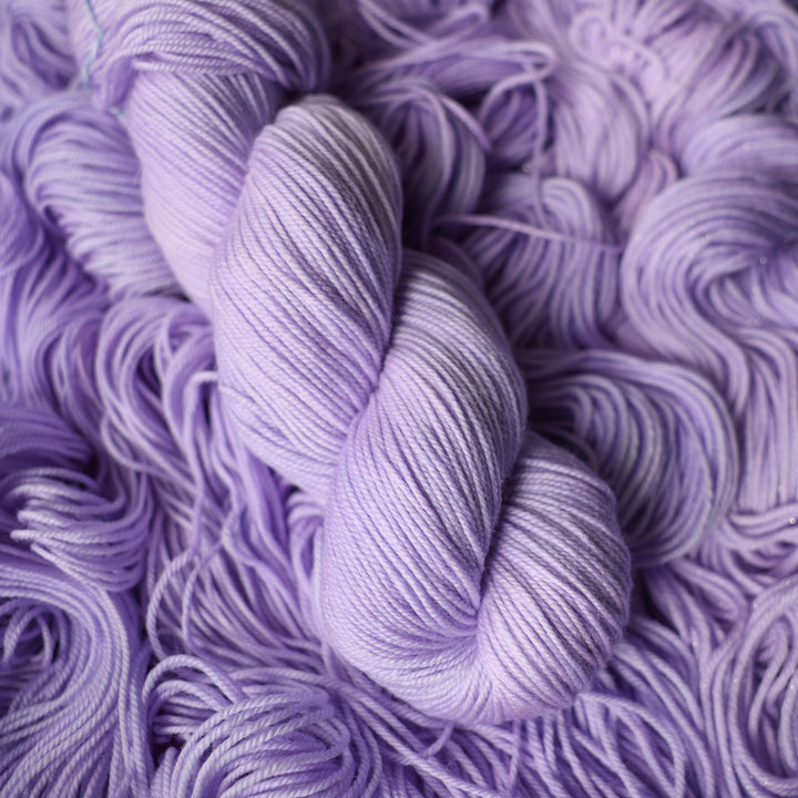 Sport yarn colored a light violet color on top of unwound skeins of this same color way.