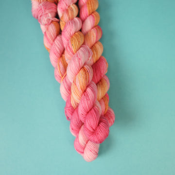 A couple of Fingering mini yarn skeins that are colored with a light pink, yellow, and orang e, on top of a light blue background.