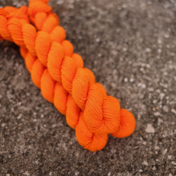 A couple of vibrant orange Fingering mini yarn skeins on top of gravel.
