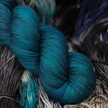 a dark ocean navy blue fingering yarn on top of unwound black white and blue yarn.