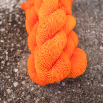 A couple of vibrant orange Fingering yarn skeins on top of gravel.