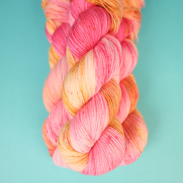 A couple of Fingering yarn skeins that are colored with a light pink, yellow, and orang e, on top of a light blue background.