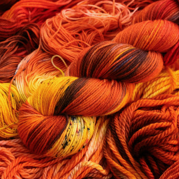 A bright red and orange colored DK yarn that has hints of purple and white and some yellow and brown colors. There are more weights of this yarn unwound underneath this skein.