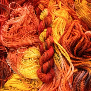 A bright red and orange colored DK mini yarn that has hints of purple and white and some yellow and brown colors. There are more weights of this yarn unwound underneath this skein.