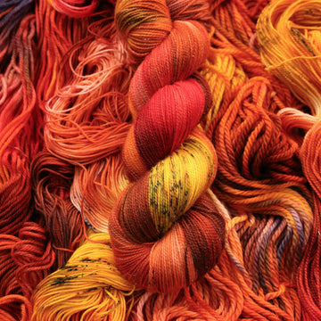 A bright red and orange colored Sparkle yarn that has hints of purple and white and some yellow and brown colors. There are more weights of this yarn unwound underneath this skein.