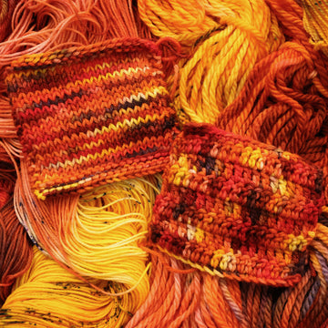 A bright red and orange colored crochet and knit swatches that have hints of purple and white and some yellow and brown colors. There are more weights of this yarn unwound underneath this skein.