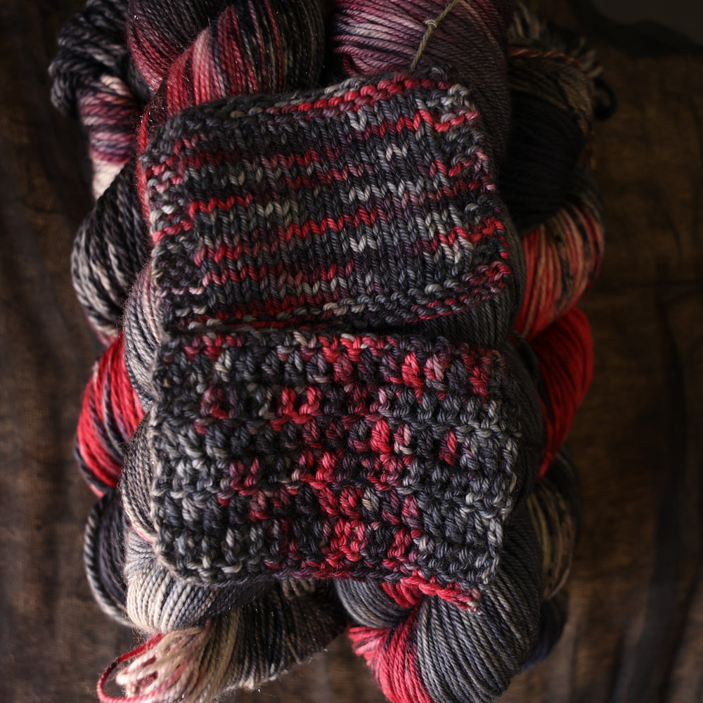 Freakin Bats knit and crochet swatch on a wooden table sitting on yarn its made of.