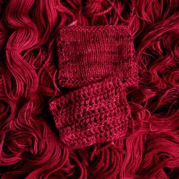 A vibrant red colored crochet and knit swatches with some dark speckles, on top of an unwound version of that same yarn.