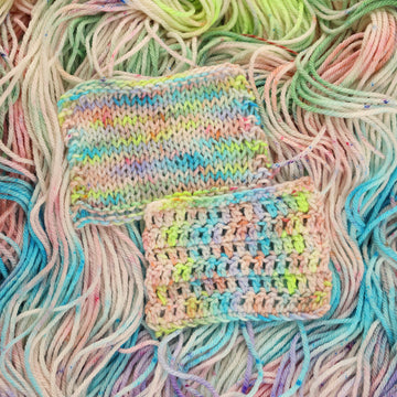 Multi colored light pastel colored knit and crochet swatches yarn with more unwound multi colored light pastel colored yarn underneath.