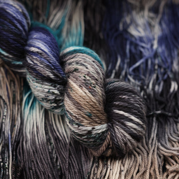 dark grey, light blue, dark blue, with black bulky yarn and speckles of all of those same colors on it, on top of the same yarn but unwound laying flat.