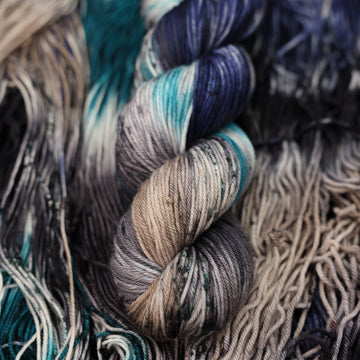 dark grey, light blue, dark blue, with black DK yarn and speckles of all of those same colors on it, on top of the same yarn but unwound laying flat.
