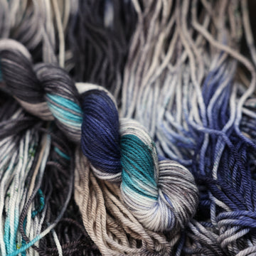 dark grey, light blue, dark blue, with black F-mini yarn and speckles of all of those same colors on it, on top of the same yarn but unwound laying flat.