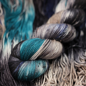 dark grey, light blue, dark blue, with black sparkle yarn and speckles of all of those same colors on it, on top of the same yarn but unwound laying flat.