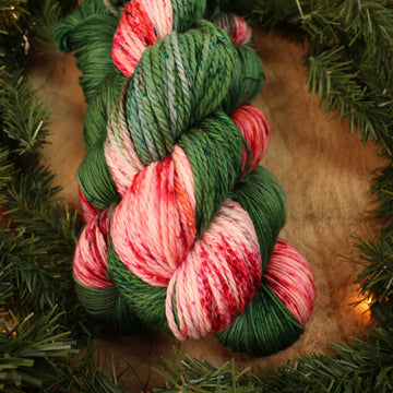 Green and red holiday bulky yarn on a wooden table with Christmas garland surrounding it.