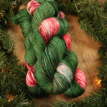Green and red holiday DK yarn on a wooden table with Christmas garland surrounding it.