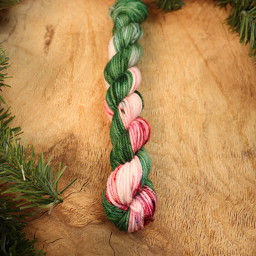 Green and red DK mini yarn on a wooden table with Christmas garland surrounding it.