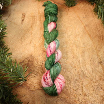 Green and red holiday mini fingering yarn on a wooden table with Christmas garland surrounding it.