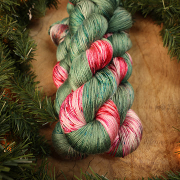 Green and red holiday silk yarn on a wooden table with Christmas garland surrounding it.