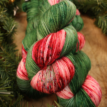 Green and red holiday sparkle yarn on a wooden table with Christmas garland surrounding it.