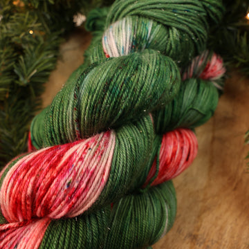Green and red holiday sparkle DK yarn on a wooden table with Christmas garland surrounding it.