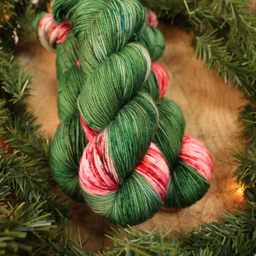 Green and red holiday sport yarn on a wooden table with Christmas garland surrounding it.