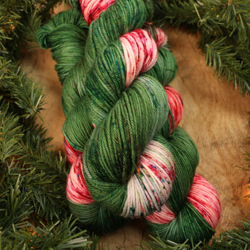 Green and red holiday worsted yarn on a wooden table with Christmas garland surrounding it.