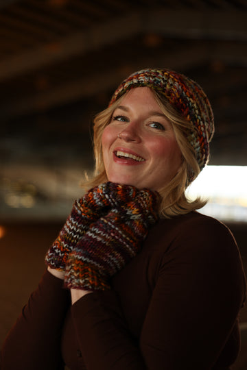 A women wearing hand knit mittens and hat that are fall colors.