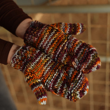A person wearing hand knit mittens that are fall colors.