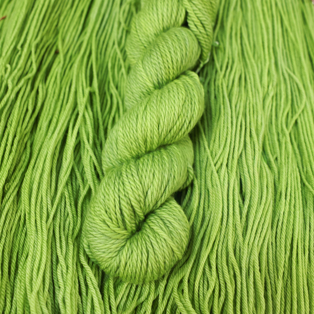 Bulky yarn colored a light bright green that is on top of an unwound skein of the same color.