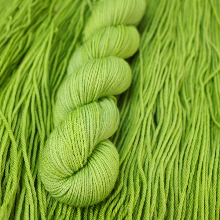 DK yarn colored a light bright green that is on top of an unwound skein of the same color.