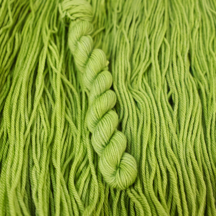 DK mini yarn colored a light bright green that is on top of an unwound skein of the same color.